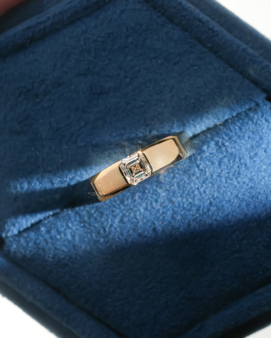 Asscher cut lab grown diamond ring in a wide yellow gold band with bezel setting, resting in a blue velvet ring box