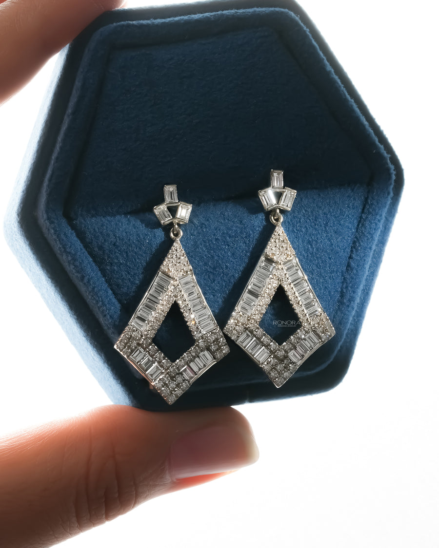 Pair of baguette lab grown diamond drop earrings in white gold shown in a blue velvet jewelry box held in hand