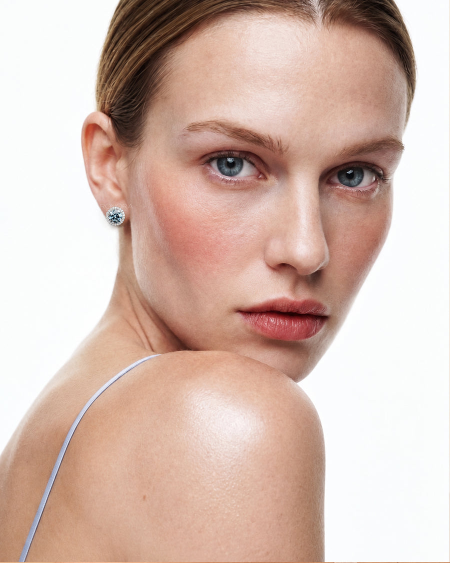 Model wearing a blue lab grown diamond halo stud earring in white gold, bare shoulder portrait on white