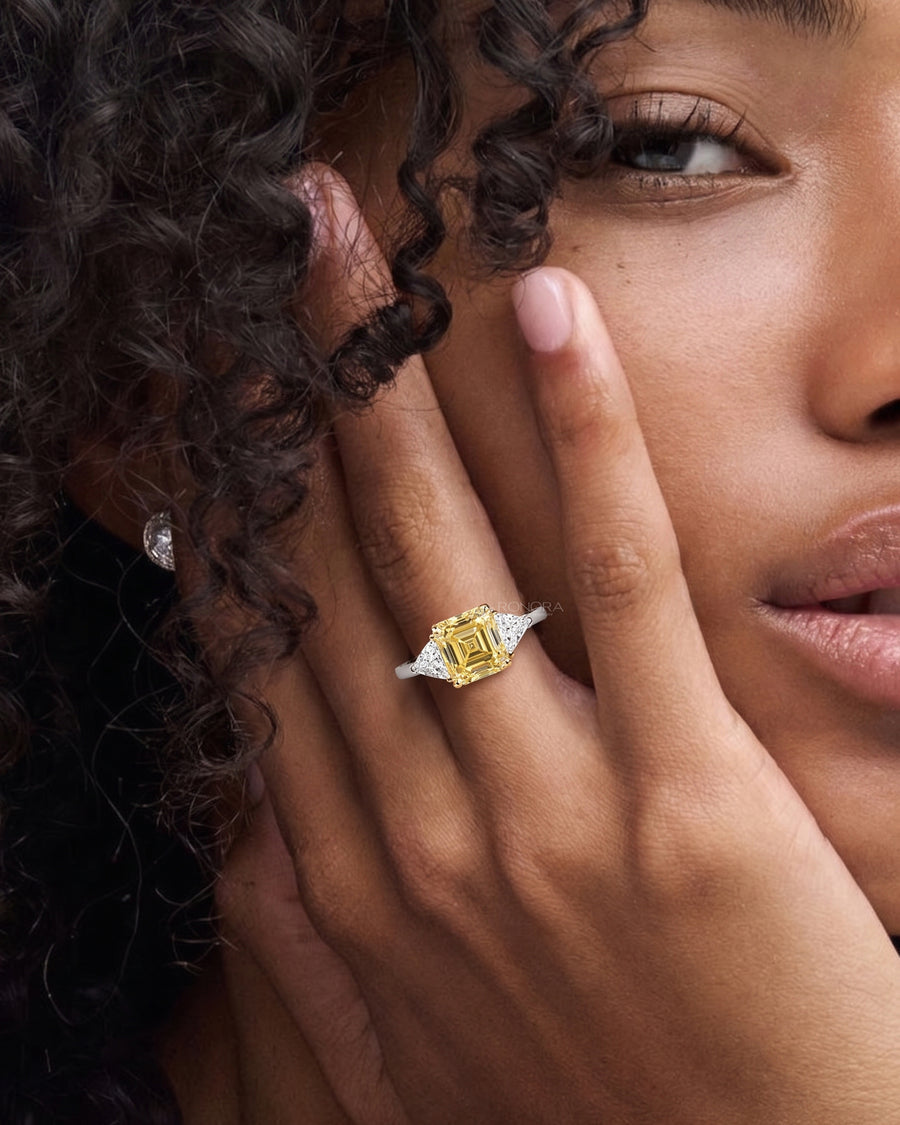 Model wearing a fancy yellow lab grown diamond ring with side stones, hand resting against her face