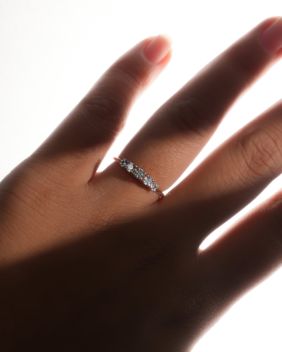 Five stone lab grown diamond pinky ring with graduated round stones, worn on a hand in soft backlight