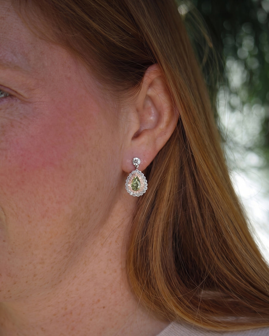 Woman wearing green pear lab grown diamond drop earrings with a pink and white diamond double halo in white gold