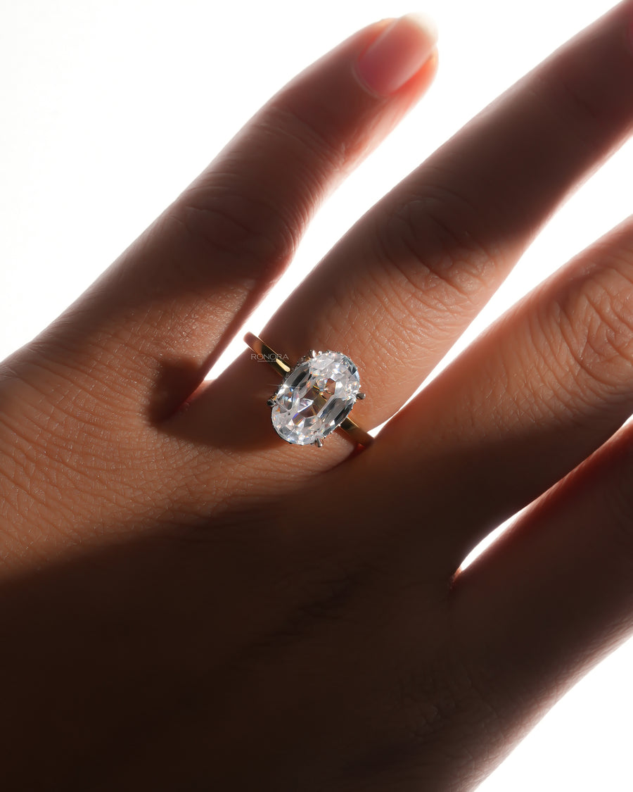Oval moissanite hidden halo ring in yellow gold worn on a hand in soft backlight with a colourless oval stone