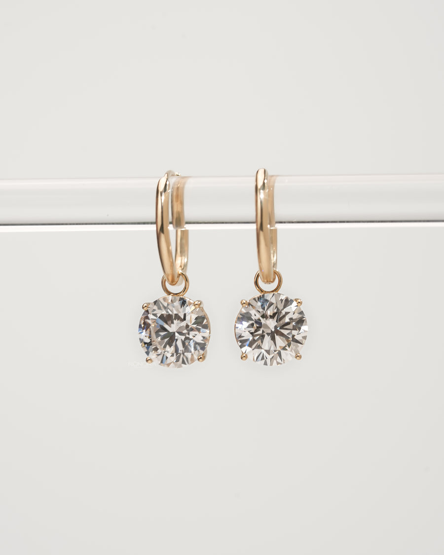 Round lab grown diamond huggie drop earrings in yellow gold hanging from a clear bar, front view