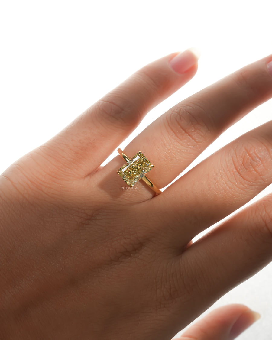 Hand wearing a yellow radiant lab grown diamond solitaire ring with a thin yellow gold band, front view