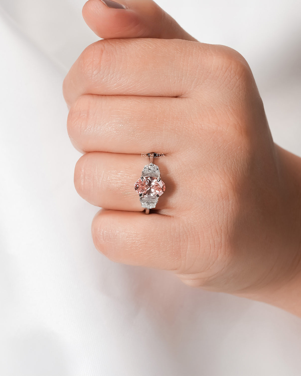 Pink lab grown diamond three-stone ring worn on hand in white metal