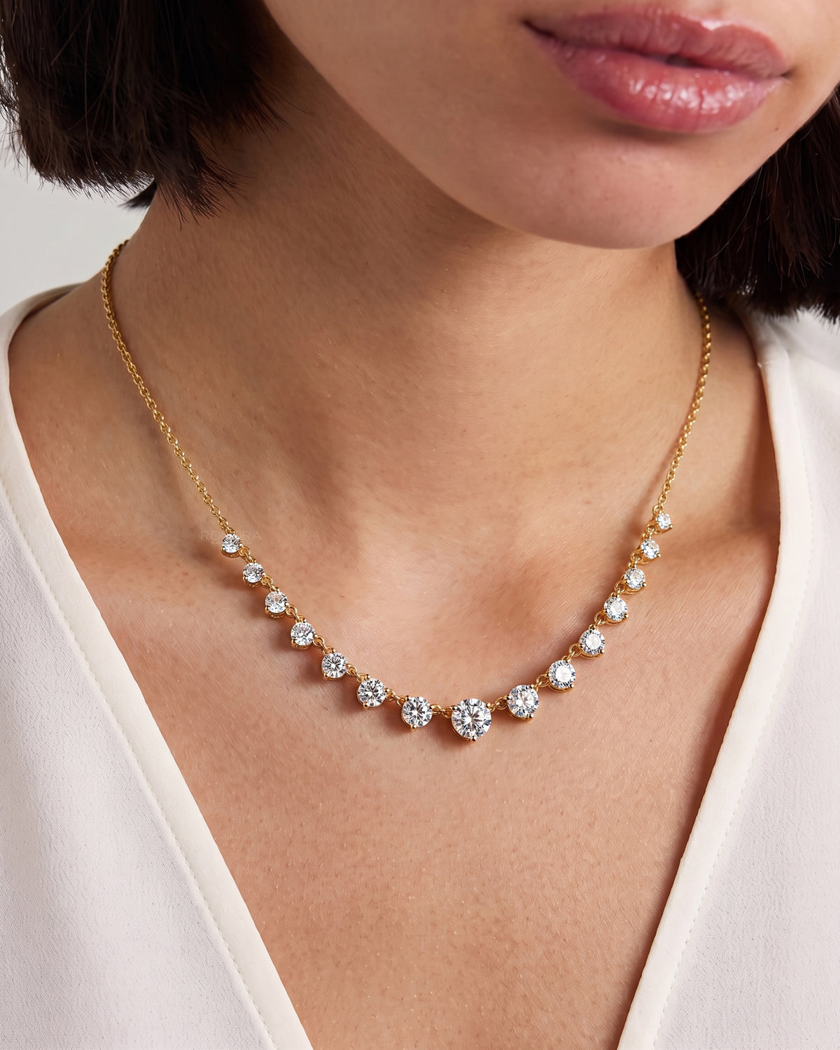 Woman wearing a yellow gold round lab grown diamond tennis necklace with graduated stones and a cream V-neck top