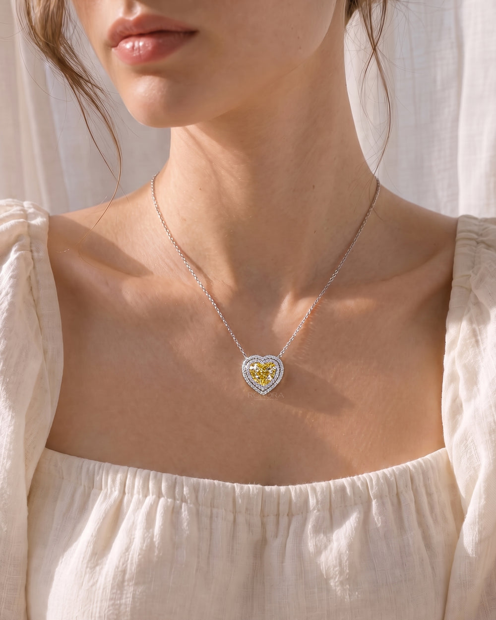 Woman wearing a yellow heart cut lab grown diamond necklace with a double halo on a white gold chain