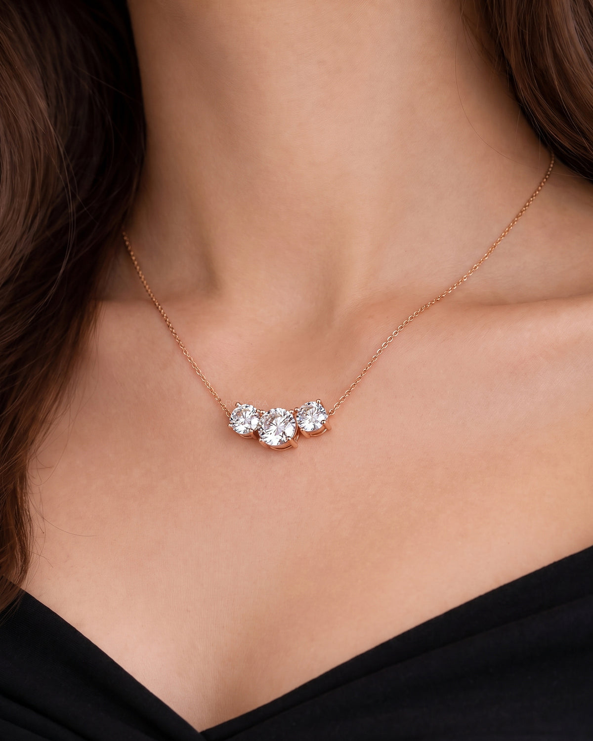 Woman wearing a three stone round lab grown diamond necklace on a fine rose gold chain with a black top