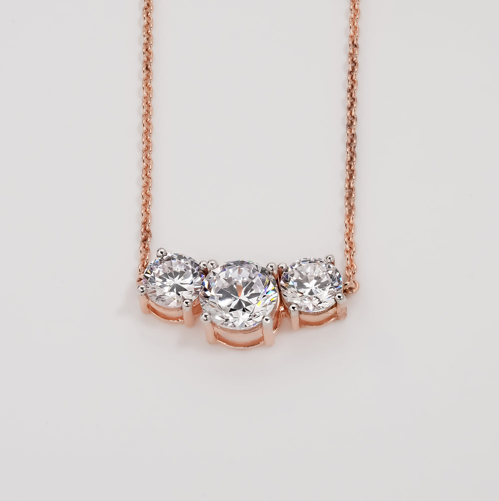Three stone round lab grown diamond necklace in rose gold on a plain light grey background, front view