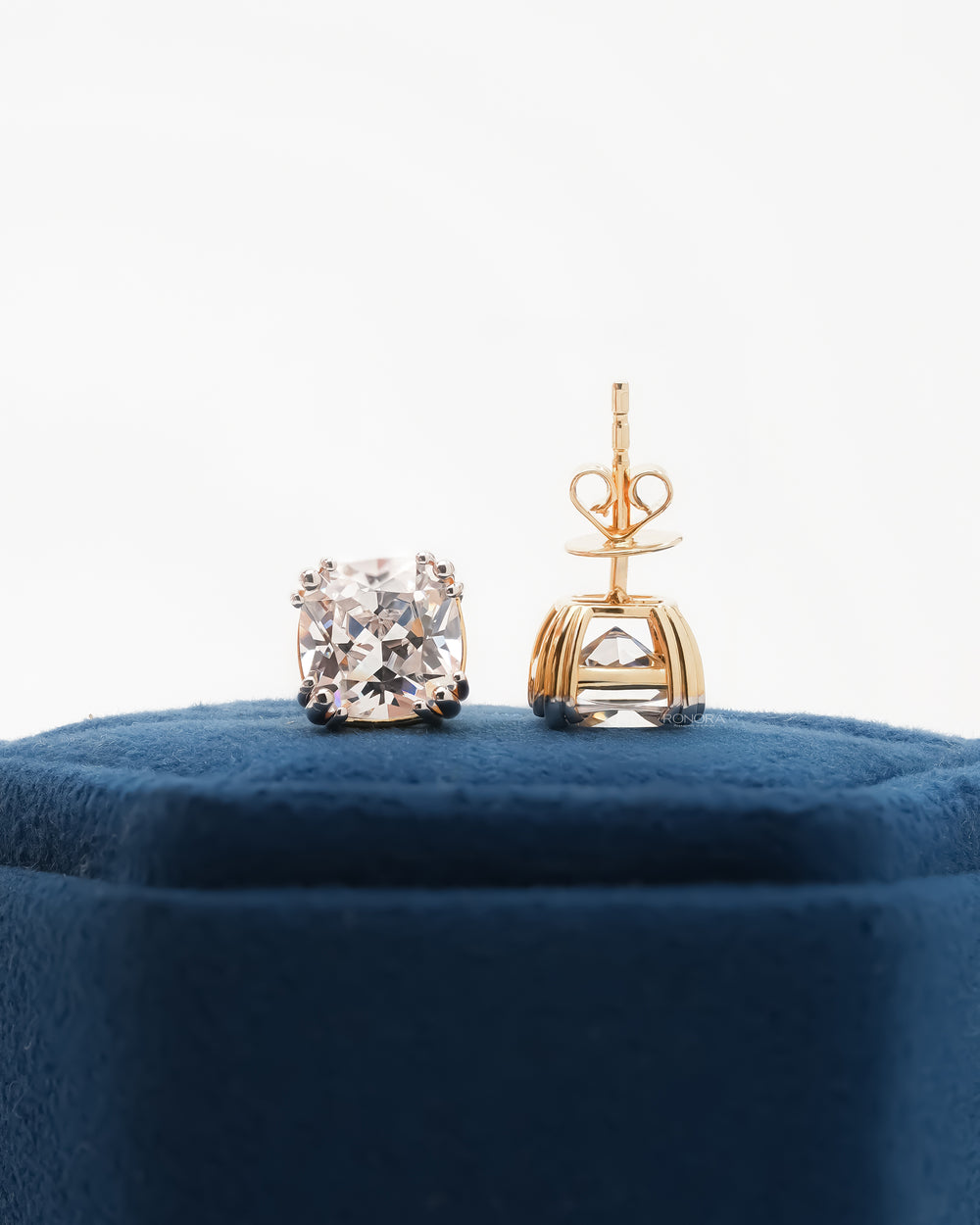 Cushion cut lab grown diamond earrings, one showing the gold post and basket back, on a blue velvet box