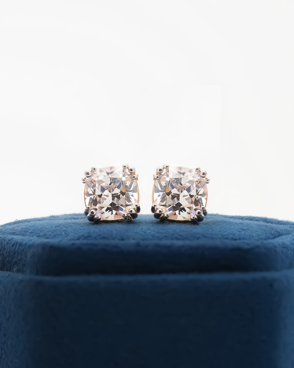 Pair of cushion cut lab grown diamond earrings with double prong settings on a blue velvet box