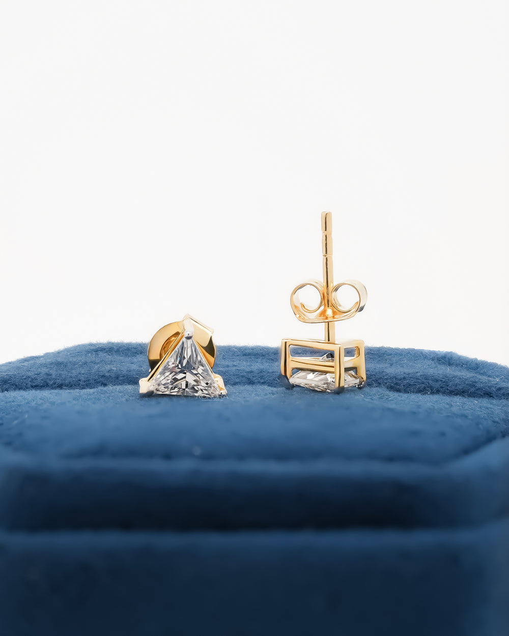 Trillion cut lab grown diamond earrings, one showing the post and butterfly back, on blue velvet