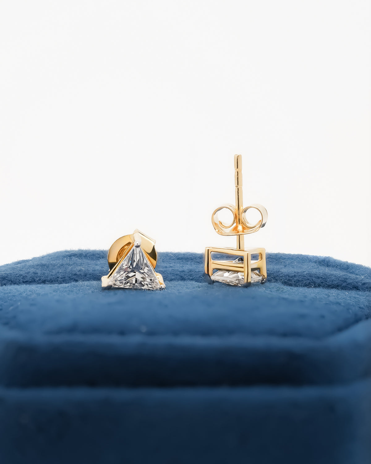 Trillion cut lab grown diamond earrings, one showing the post and butterfly back, on blue velvet
