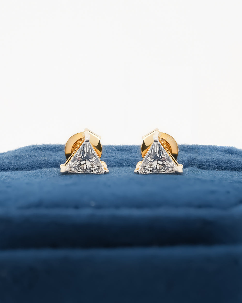Pair of trillion cut lab grown diamond earrings in yellow gold standing on a blue velvet box