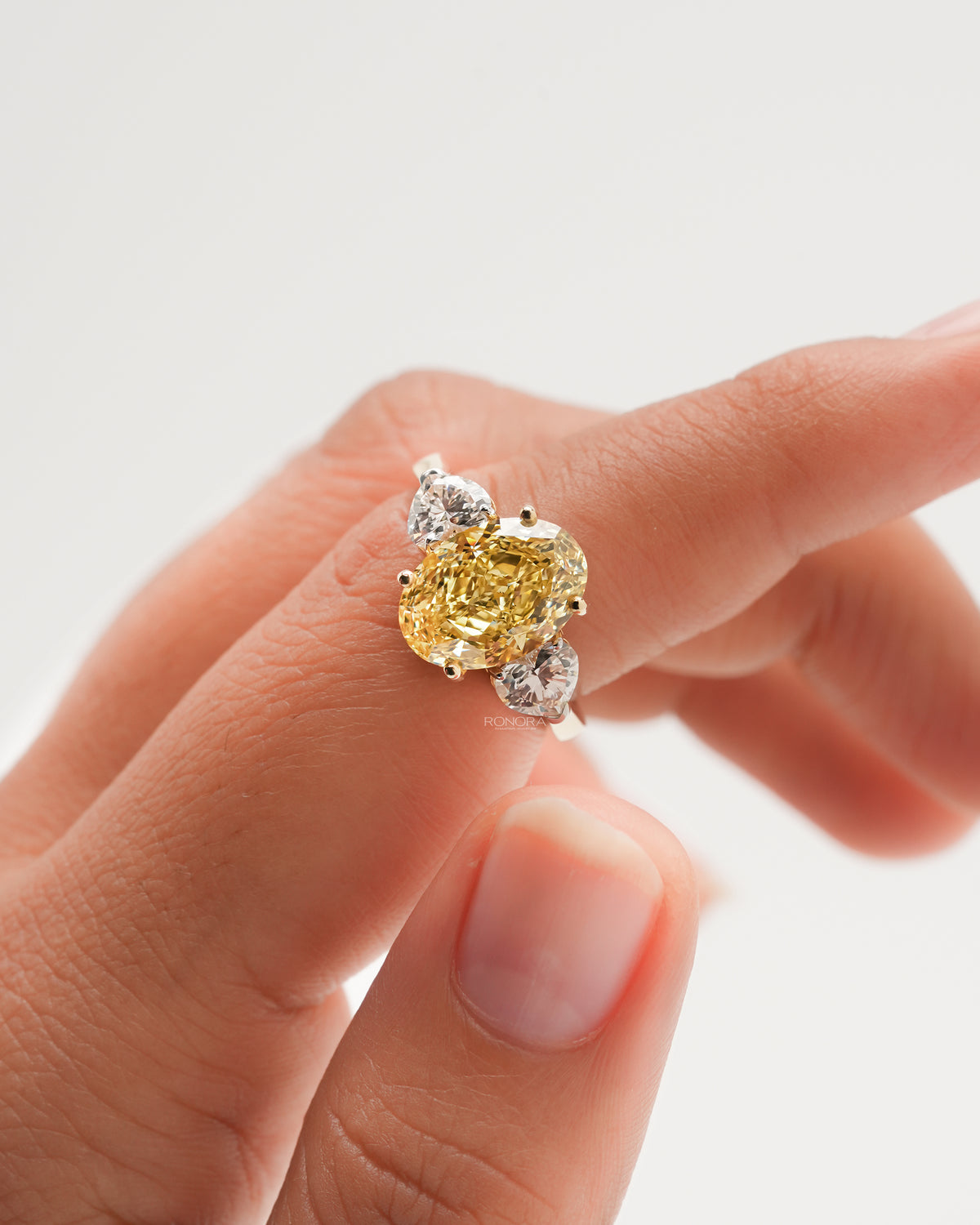 Close-up of an oval yellow lab grown diamond ring on a finger, flanked by two white heart shaped side stones
