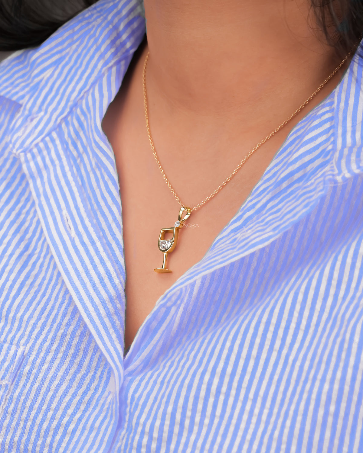 Woman wearing a small yellow gold wine glass lab grown diamond pendant over a light blue striped shirt