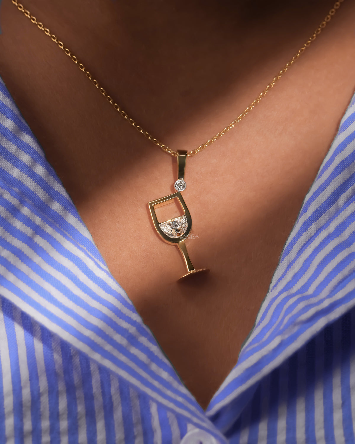 Close-up of a model wearing a yellow gold wine glass lab grown diamond pendant with a blue striped shirt