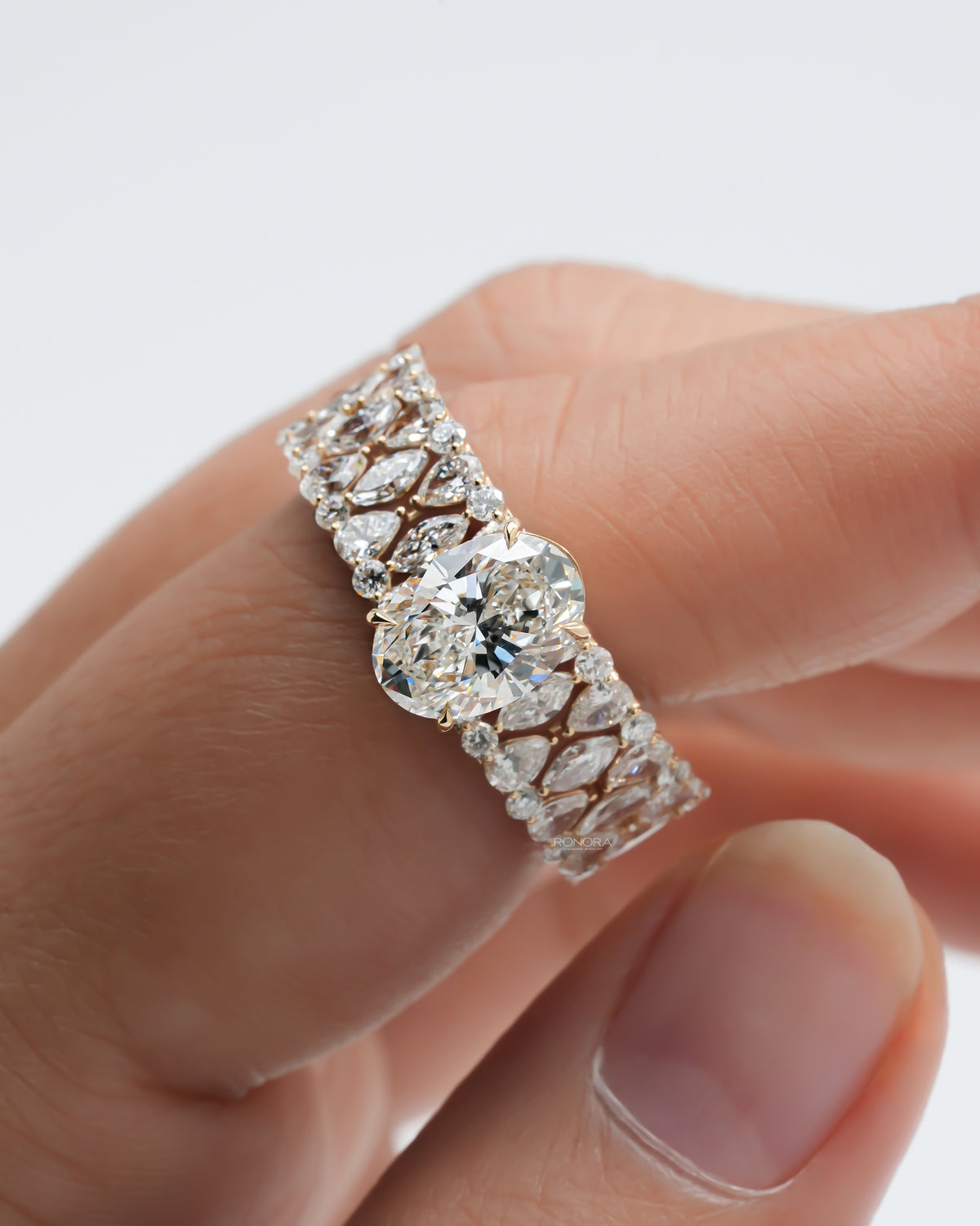 Oval cluster lab grown diamond ring held between fingers showing the open lattice band