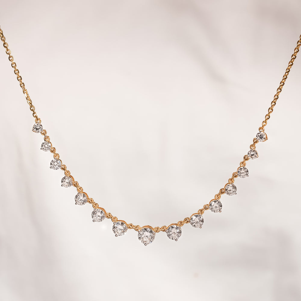 Round lab grown diamond tennis necklace in yellow gold with graduated stones against a soft cream background