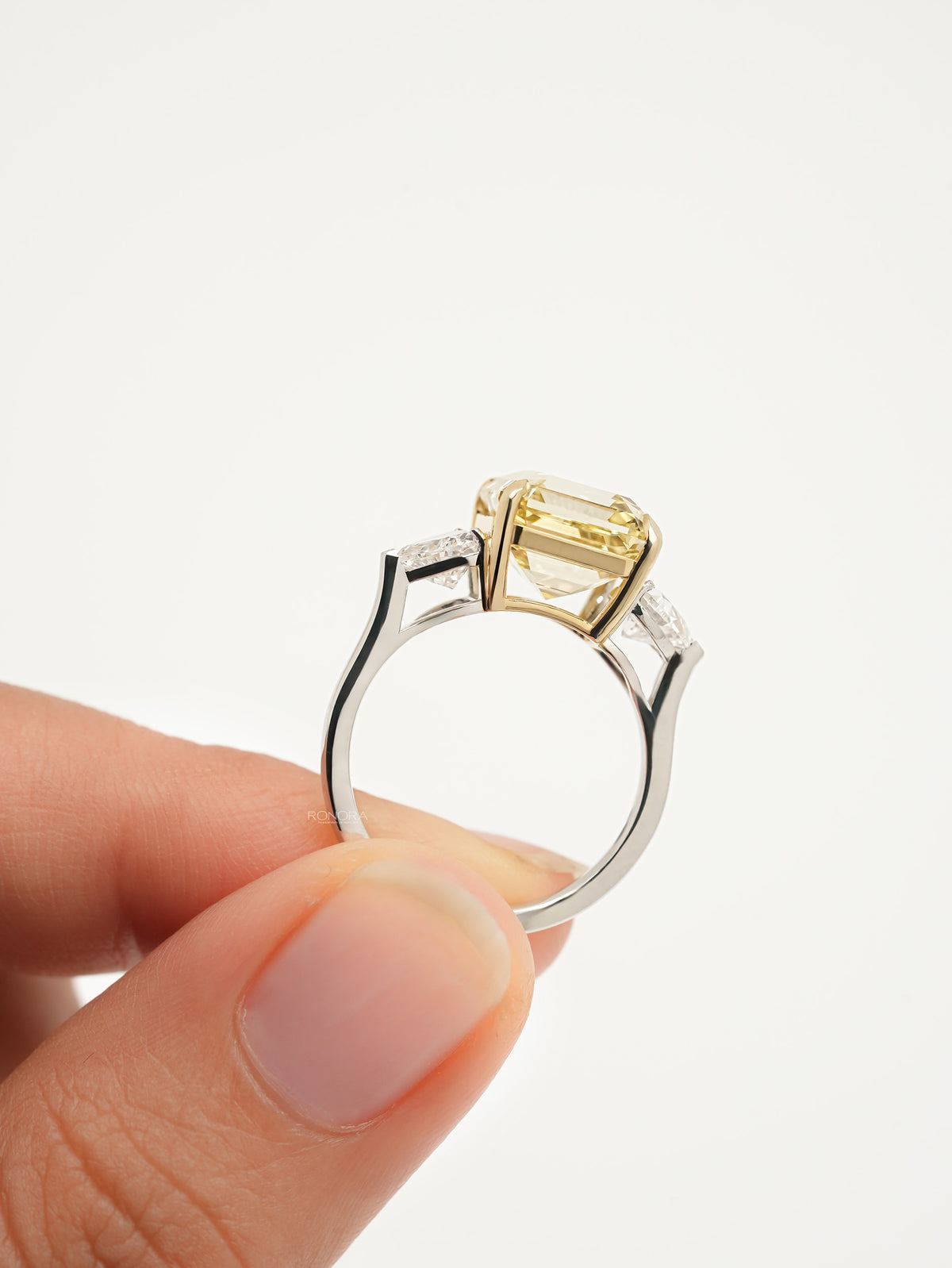 Side view of an asscher yellow lab grown diamond ring held up, yellow gold basket on a slim white metal band