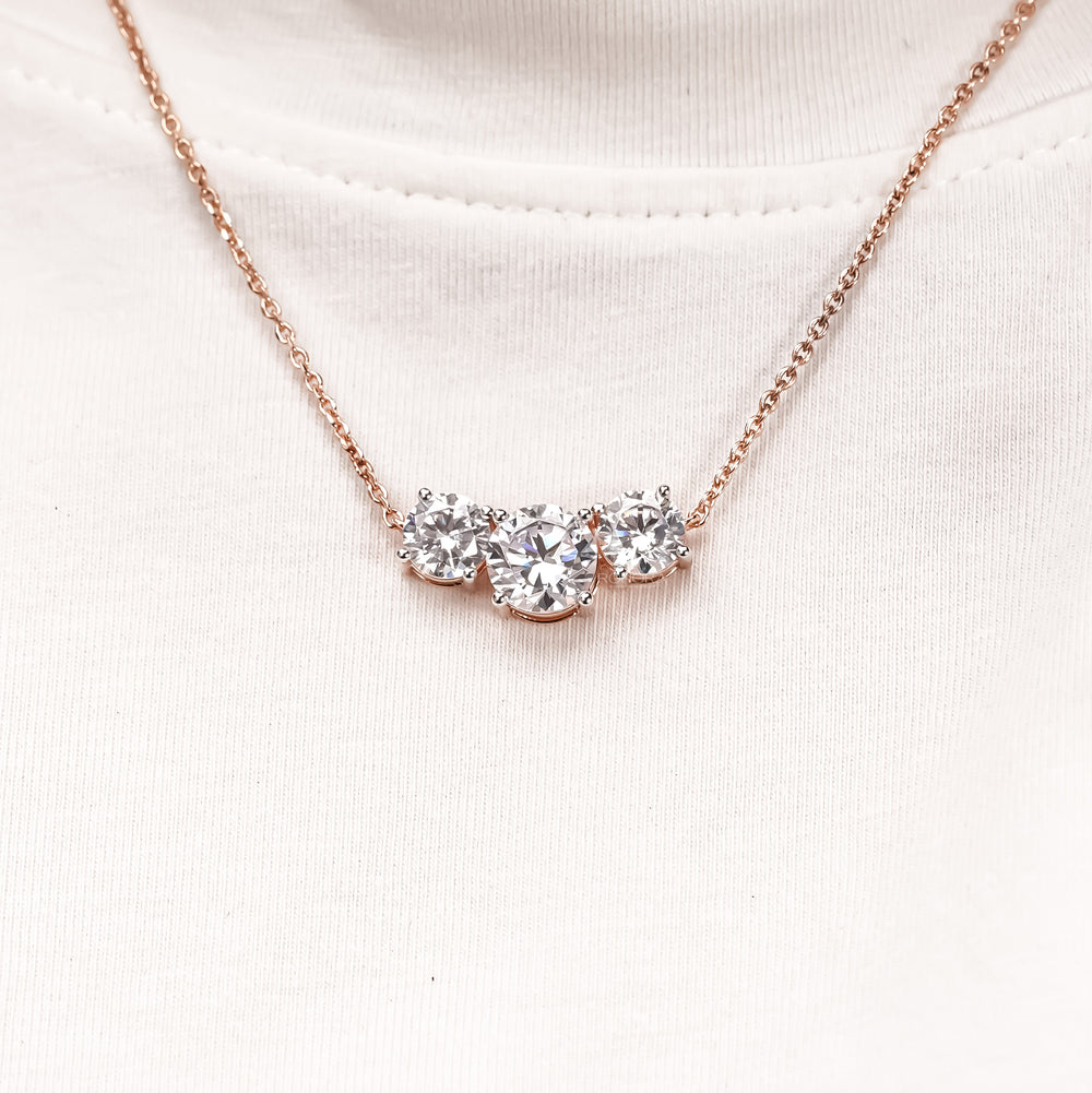 Three stone round lab grown diamond necklace in rose gold worn by a model over a white t-shirt