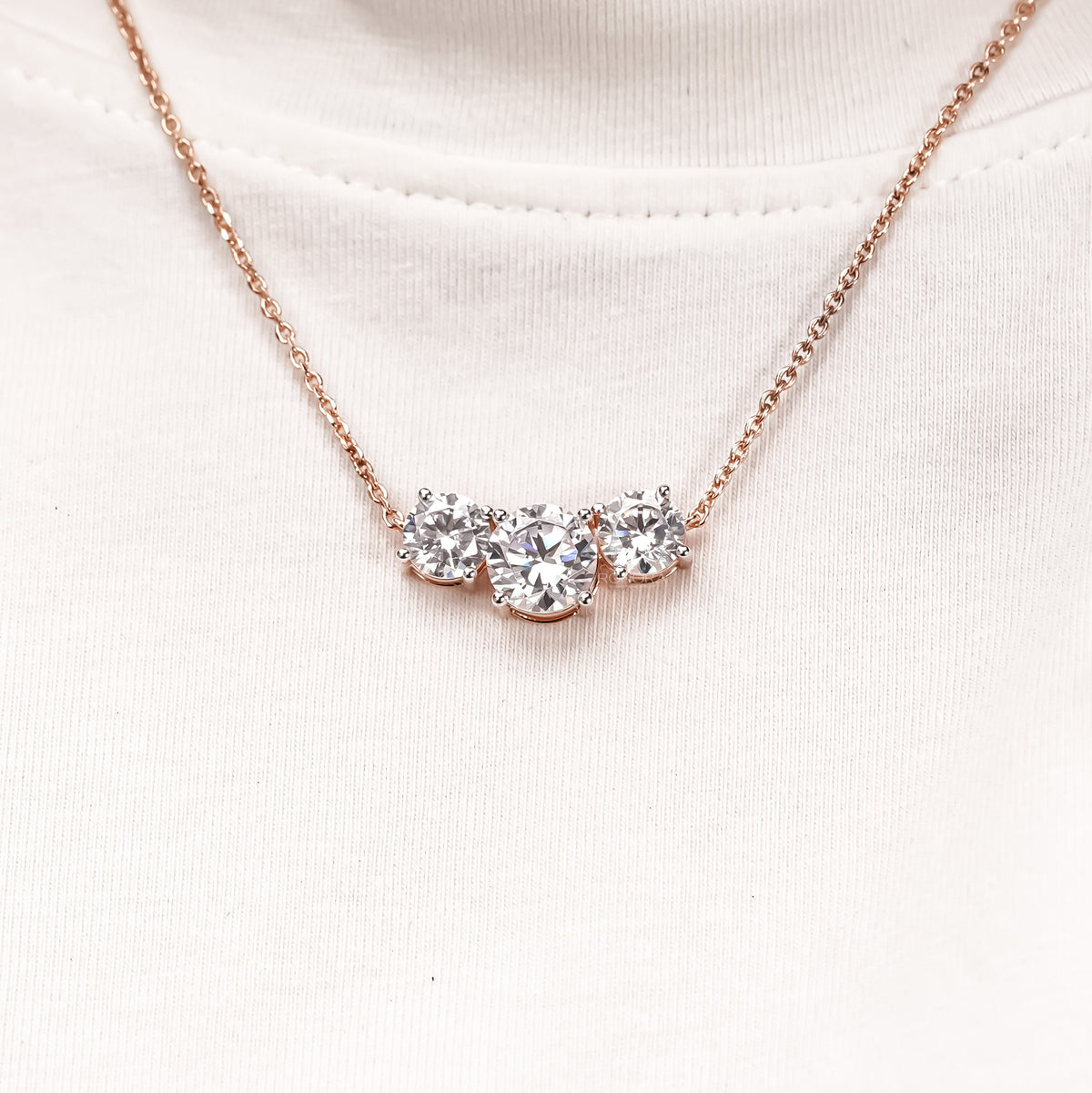 Three stone round lab grown diamond necklace in rose gold worn by a model over a white t-shirt