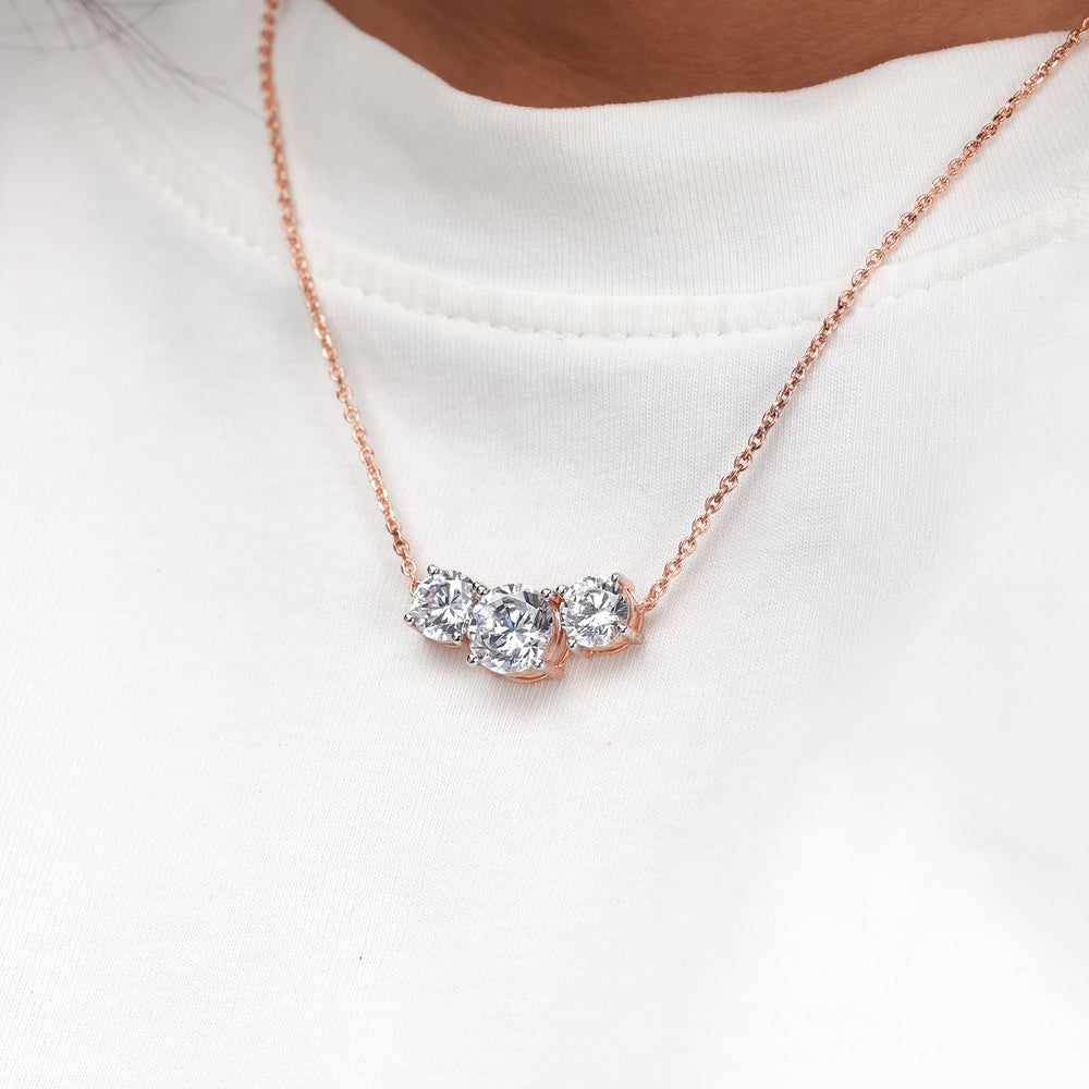 Close-up of a rose gold three stone round lab grown diamond necklace worn on a model in a white t-shirt