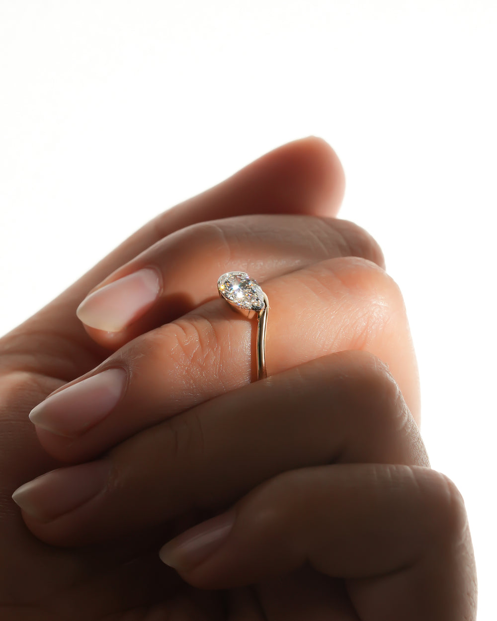 Close-up of an east west pear lab grown diamond ring sparkling on a finger, hands held in soft backlight