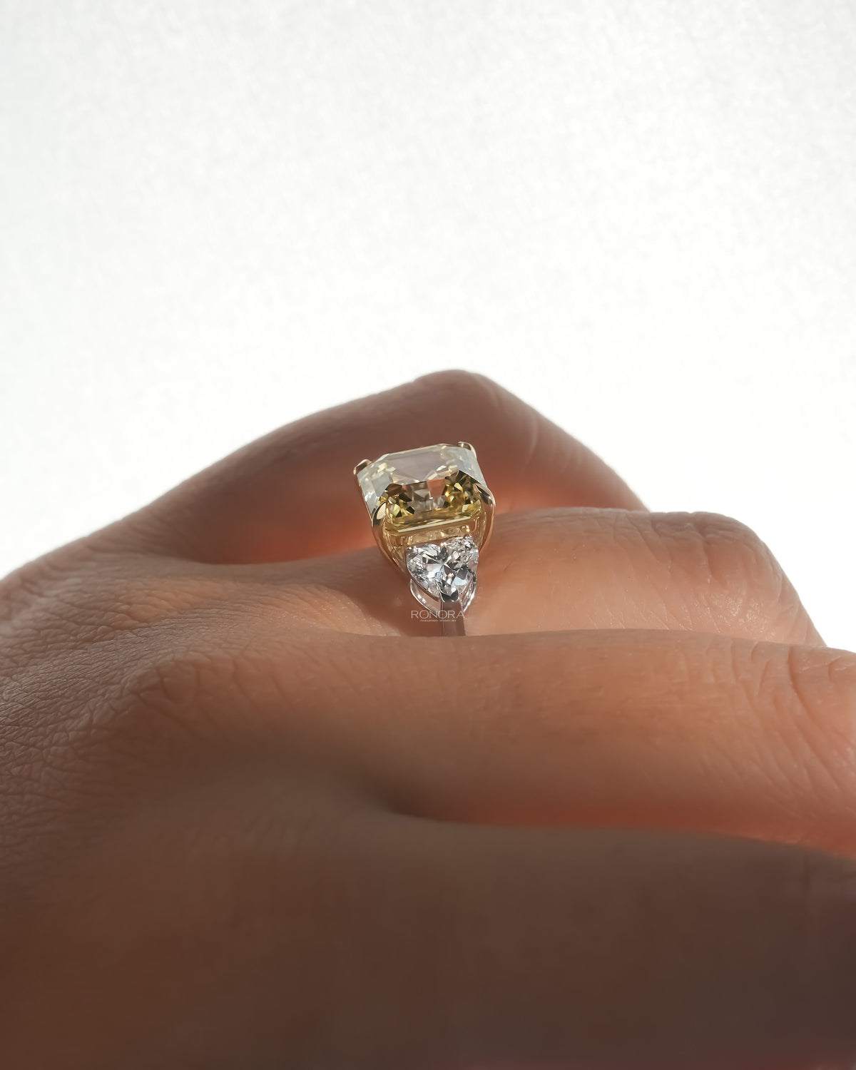 Side view of an asscher yellow lab grown diamond ring worn on a finger with a white heart shaped side stone