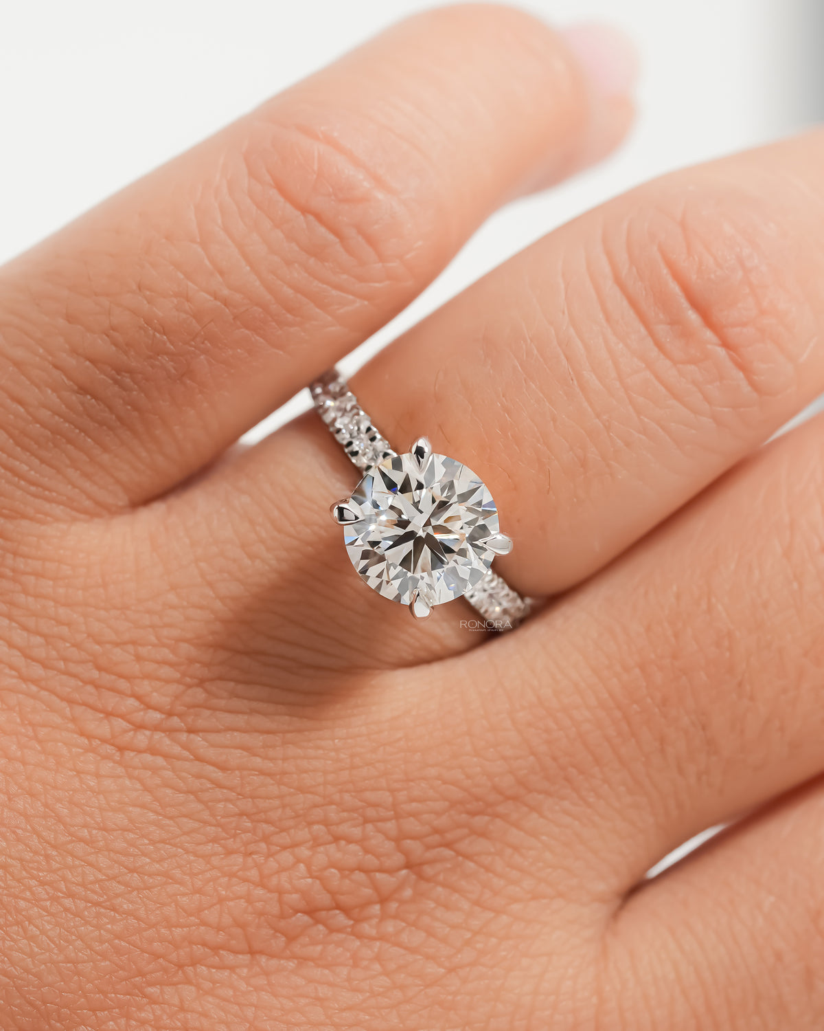 Close-up of a round hidden halo lab grown diamond ring in white gold with a diamond pave band on a finger