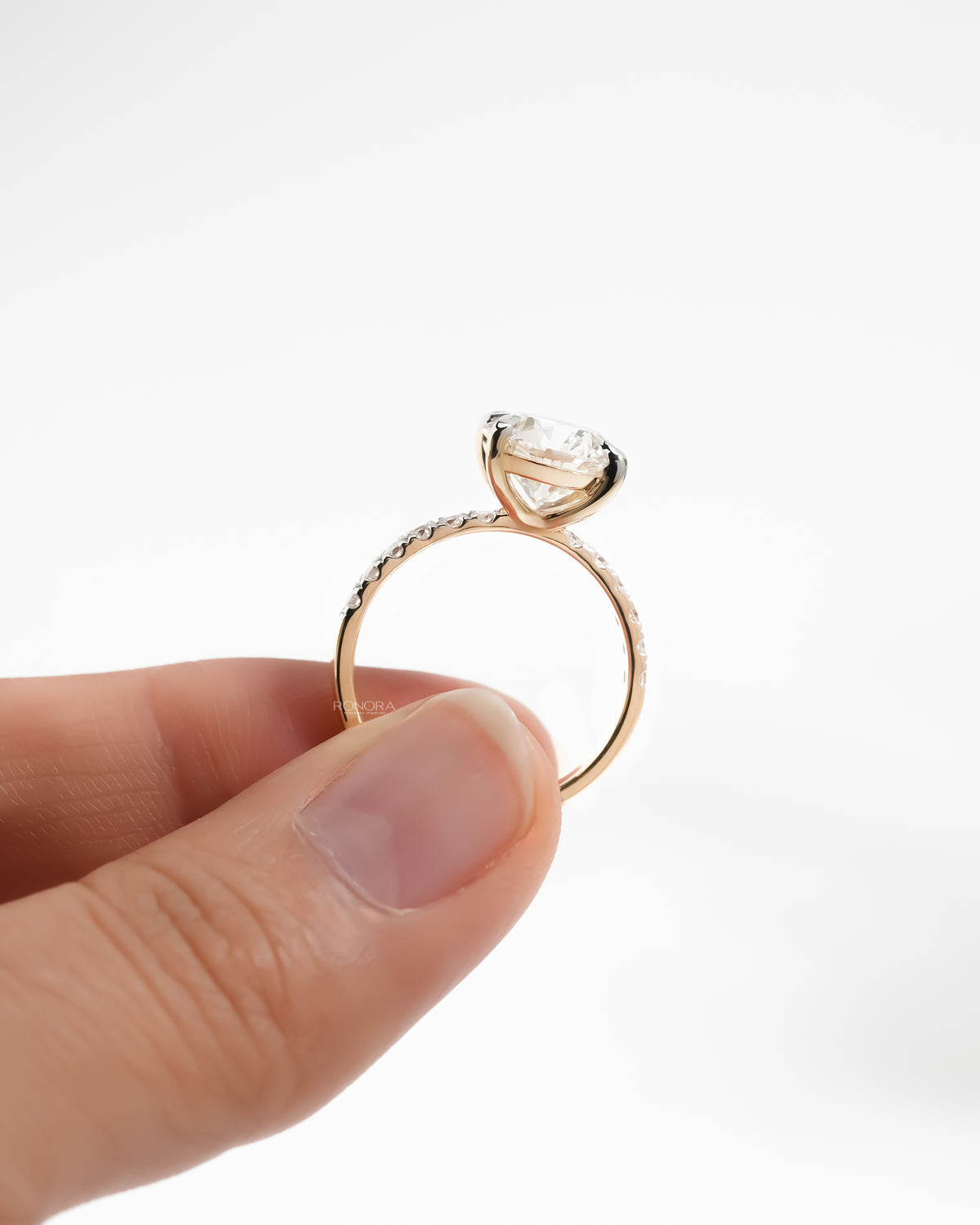 Side view of a yellow gold hidden halo lab grown diamond ring with a pave diamond band held between fingers