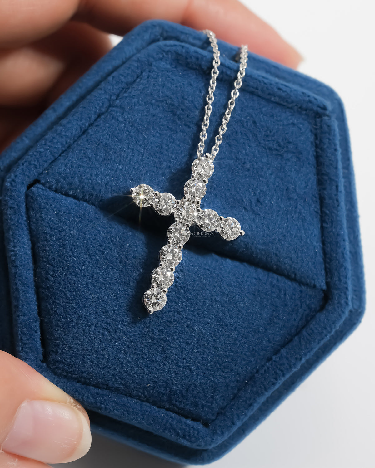 White gold cross pendant of round lab grown diamonds on a chain, in a navy velvet box