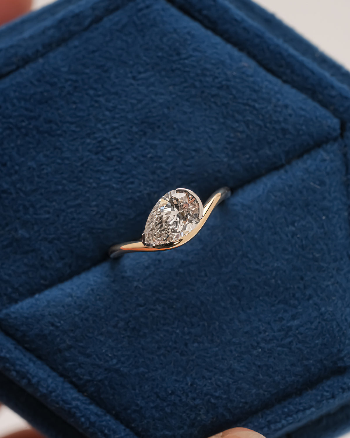 East west pear lab grown diamond ring with a curved gold band, resting in a blue velvet jewelry box