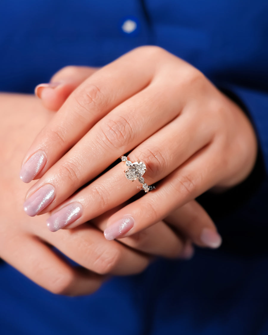 Oval lab grown diamond side-stone ring worn on hand in yellow gold