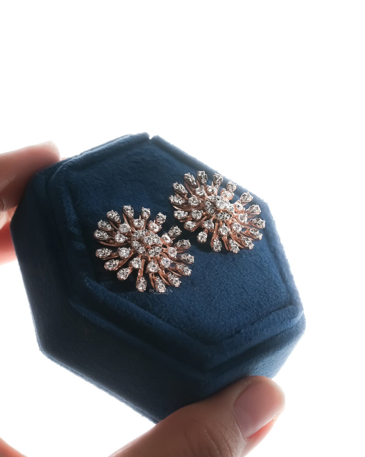 Pair of starburst cluster lab grown diamond earrings in rose gold in a blue velvet box held in hand