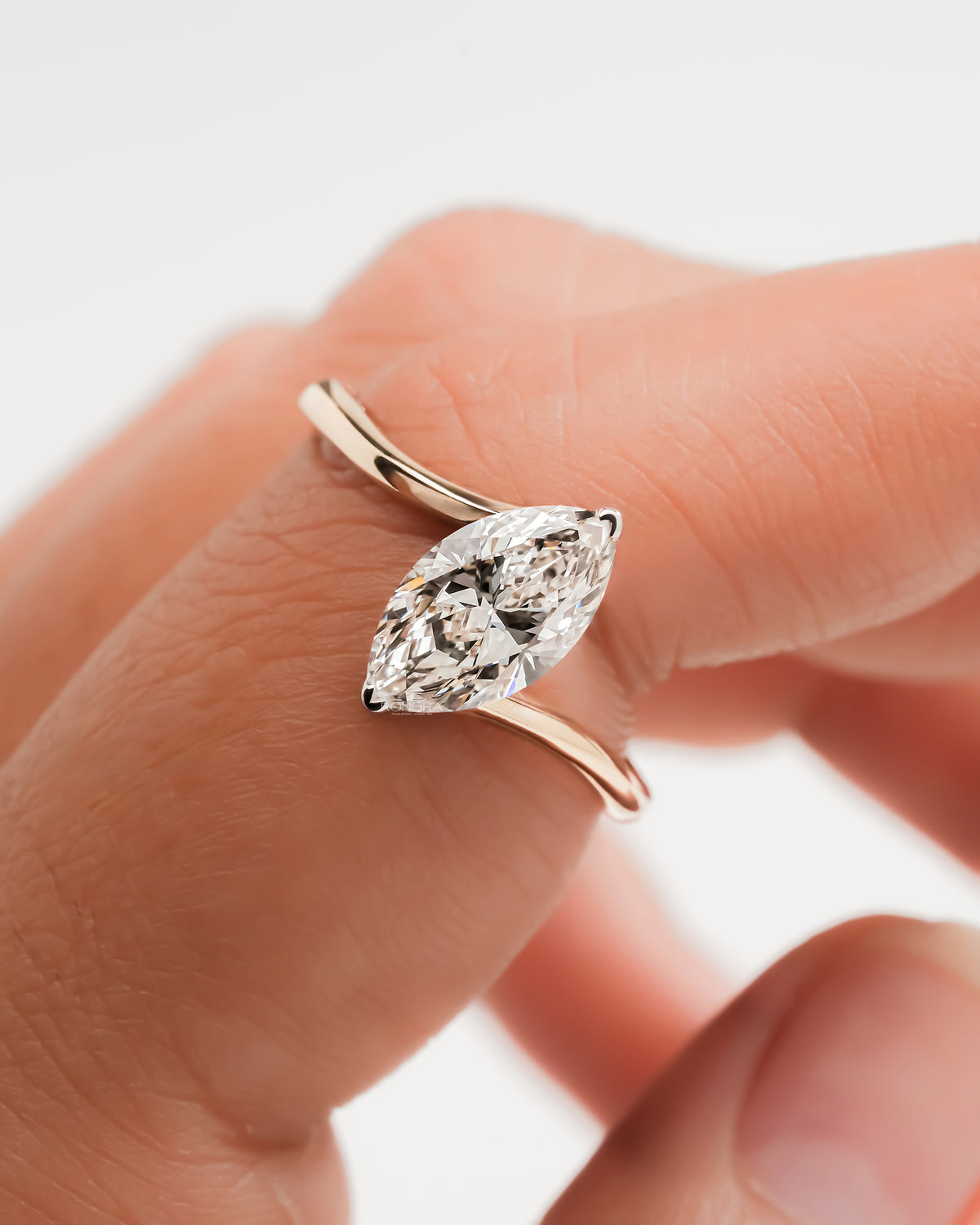 Close-up of a marquise lab grown diamond bypass ring in rose gold on a finger, showing the faceted stone
