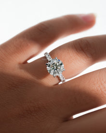 Round hidden halo lab grown diamond ring in white gold with a diamond pave band, on a softly backlit hand