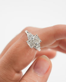 Close-up of a radiant three stone lab grown diamond ring with trapezoid side stones held on a finger
