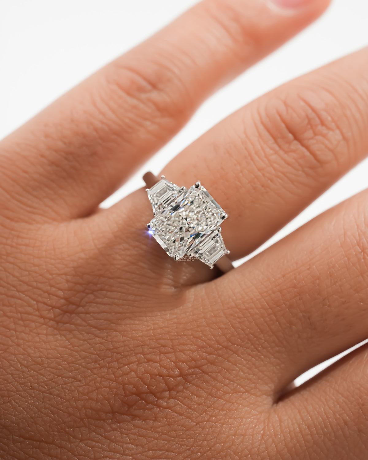 Close-up of a radiant three stone lab grown diamond ring with trapezoid side stones worn on a hand