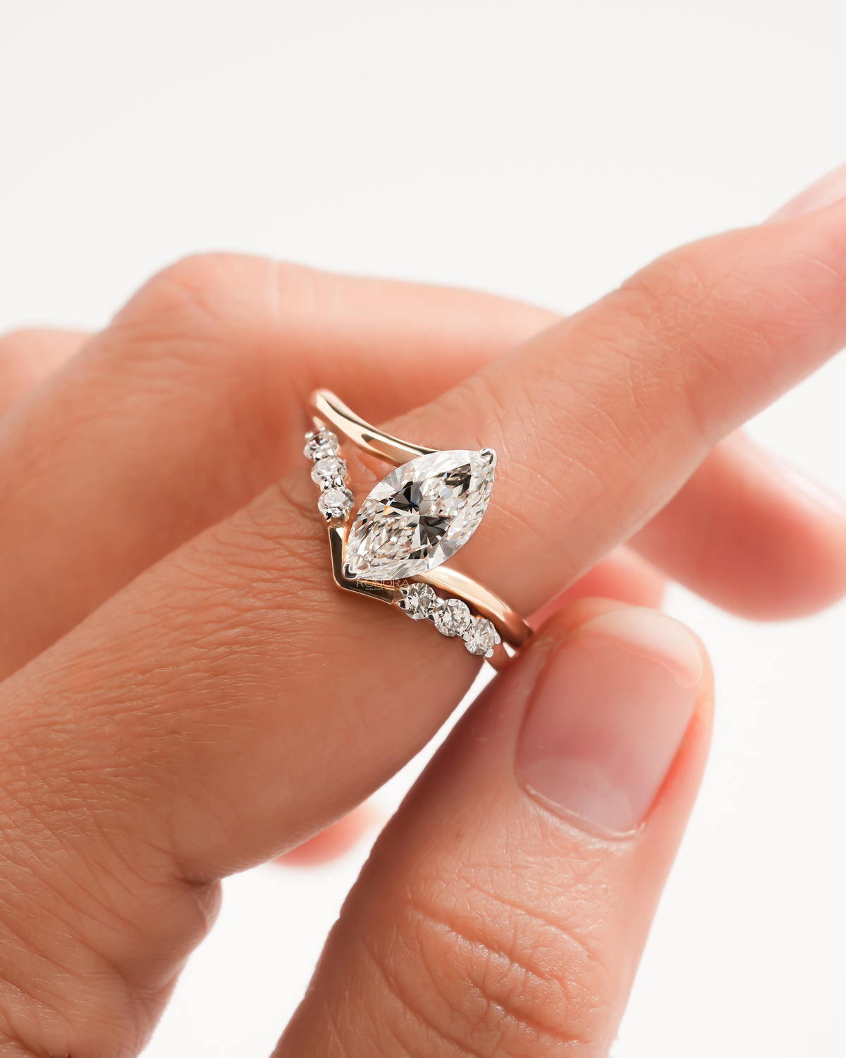 Marquise lab grown diamond ring set in rose gold with a V shaped diamond band, held between fingers