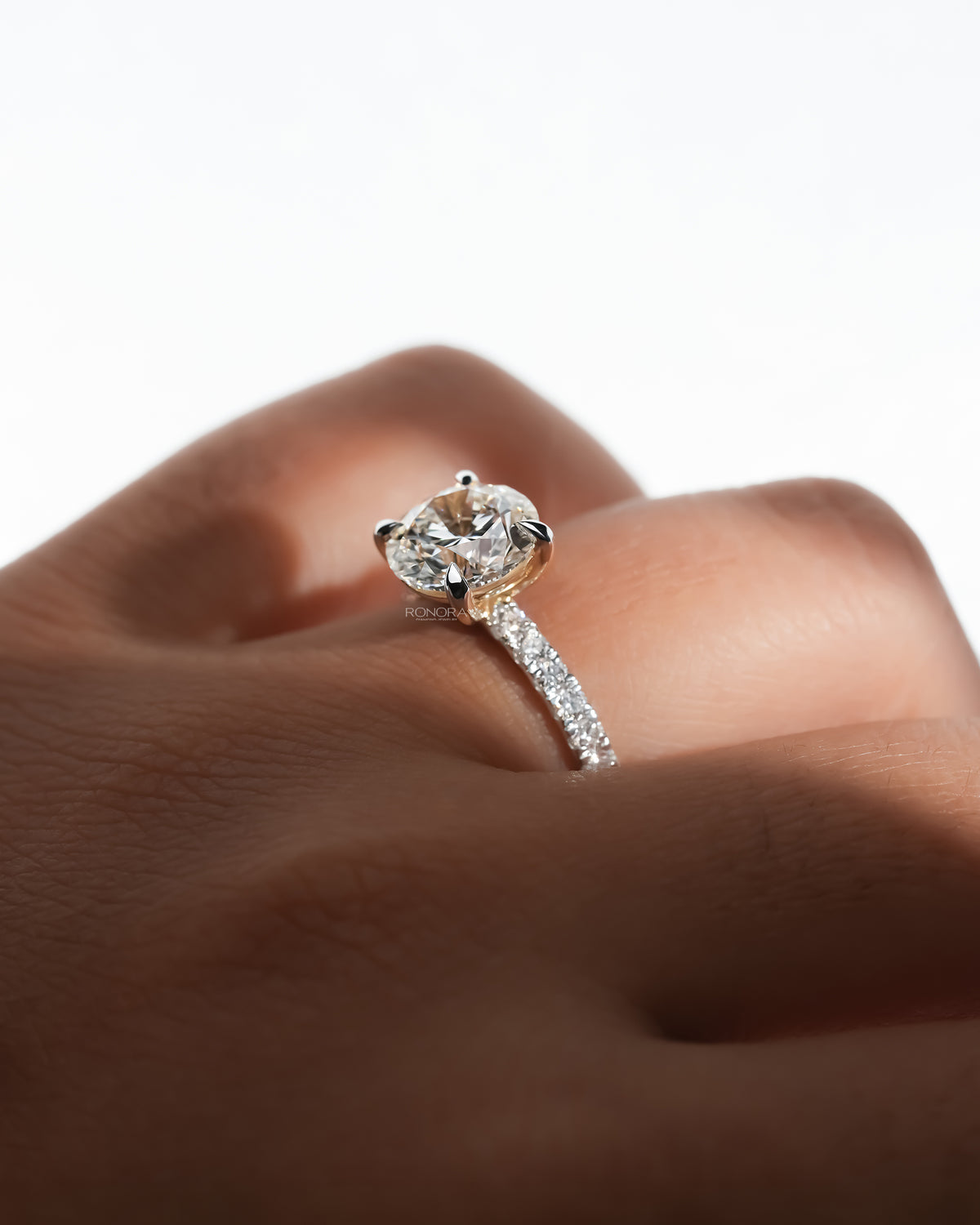 Side close-up of a round hidden halo lab grown diamond ring with a pave band worn on a finger