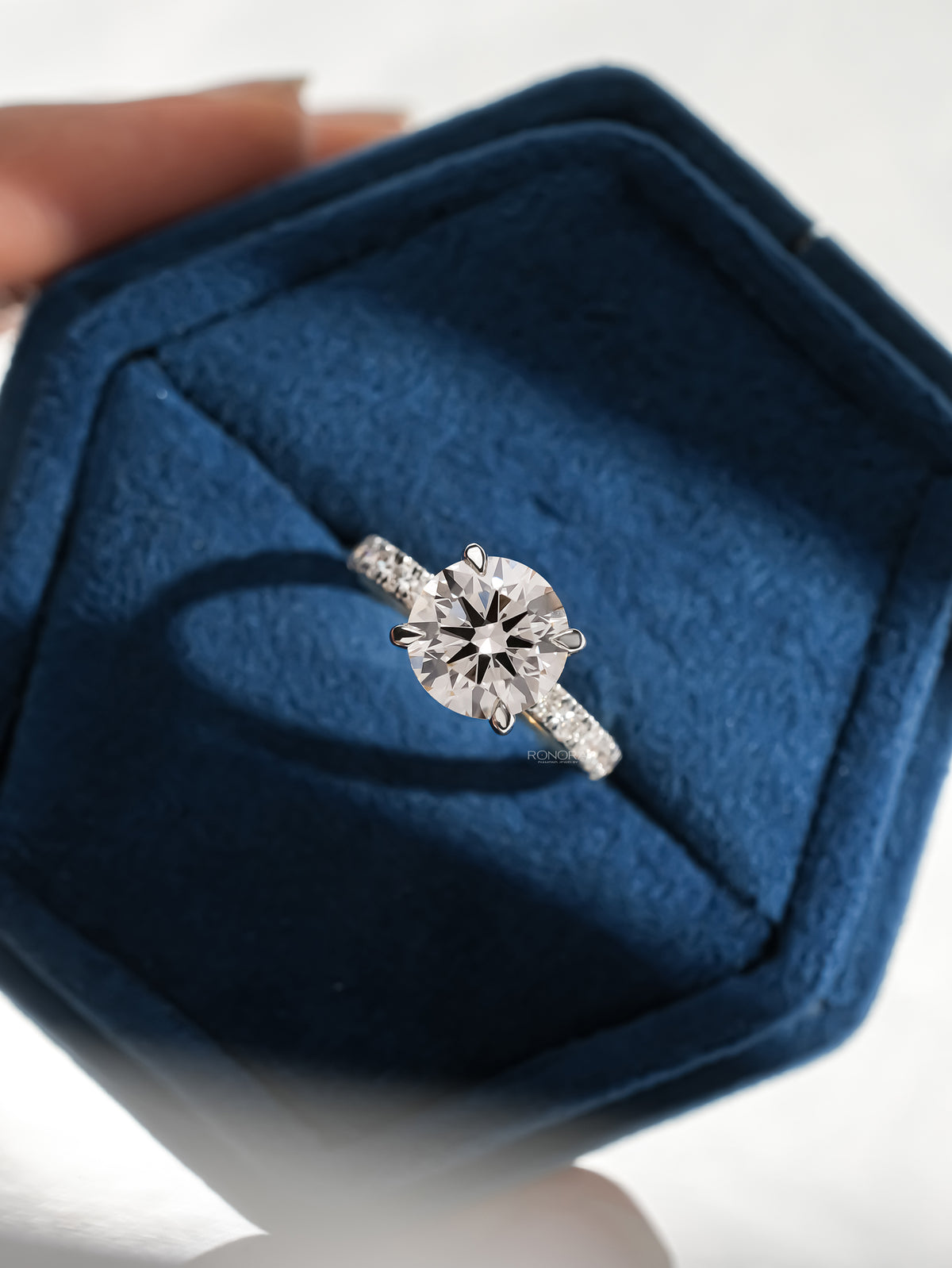 Top view of a round hidden halo lab grown diamond ring in white gold in a blue velvet ring box