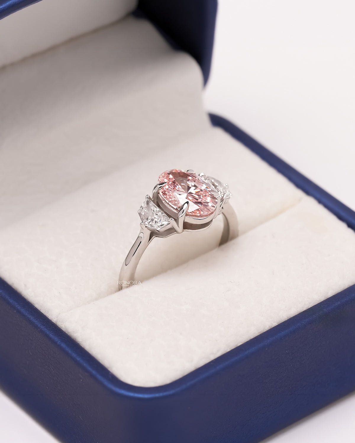 Angled view of pink lab grown diamond three-stone ring showing side-stone setting
