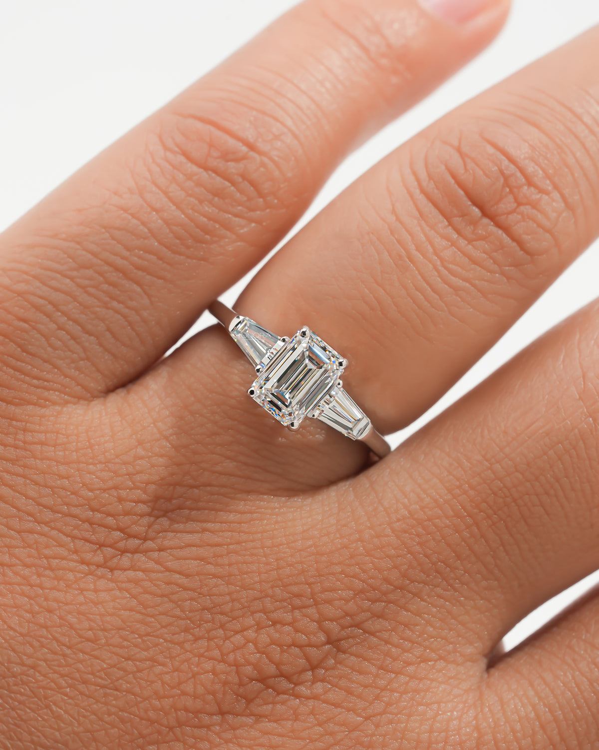 Emerald cut lab grown diamond three stone ring with white gold band and tapered side stones, worn on a hand