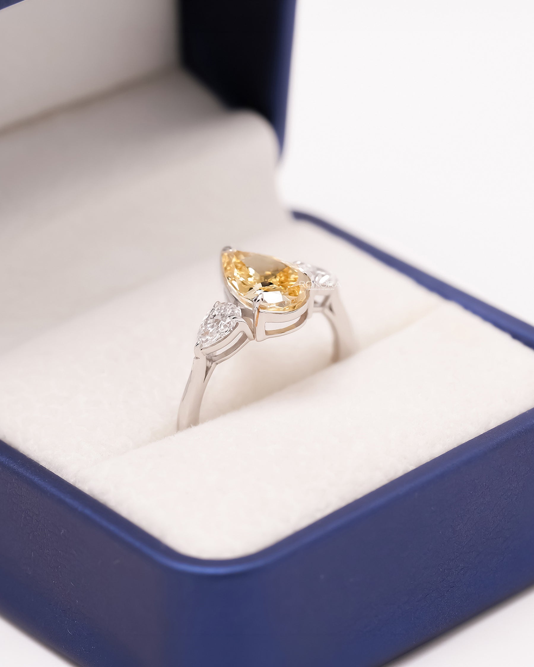 Angled view of yellow pear lab grown diamond three-stone ring showing three-stone setting