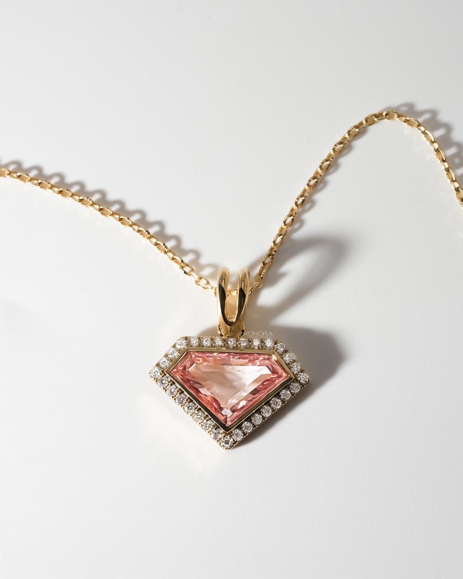 Pink shield cut lab grown diamond necklace with a halo of white stones on a yellow gold chain, flat on white