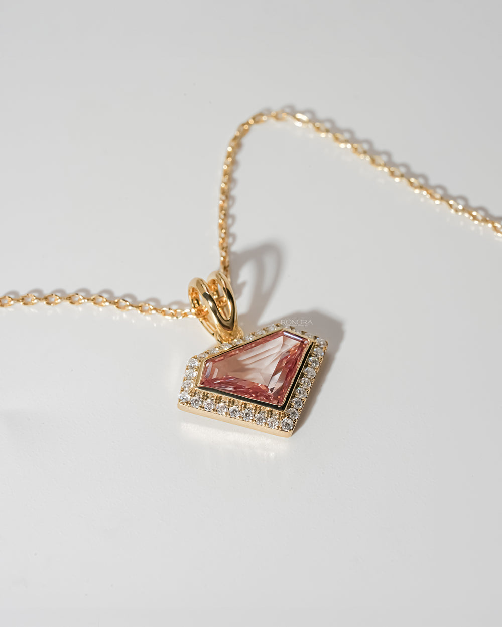 Angled view of a pink shield cut lab grown diamond necklace with a white stone halo and yellow gold chain