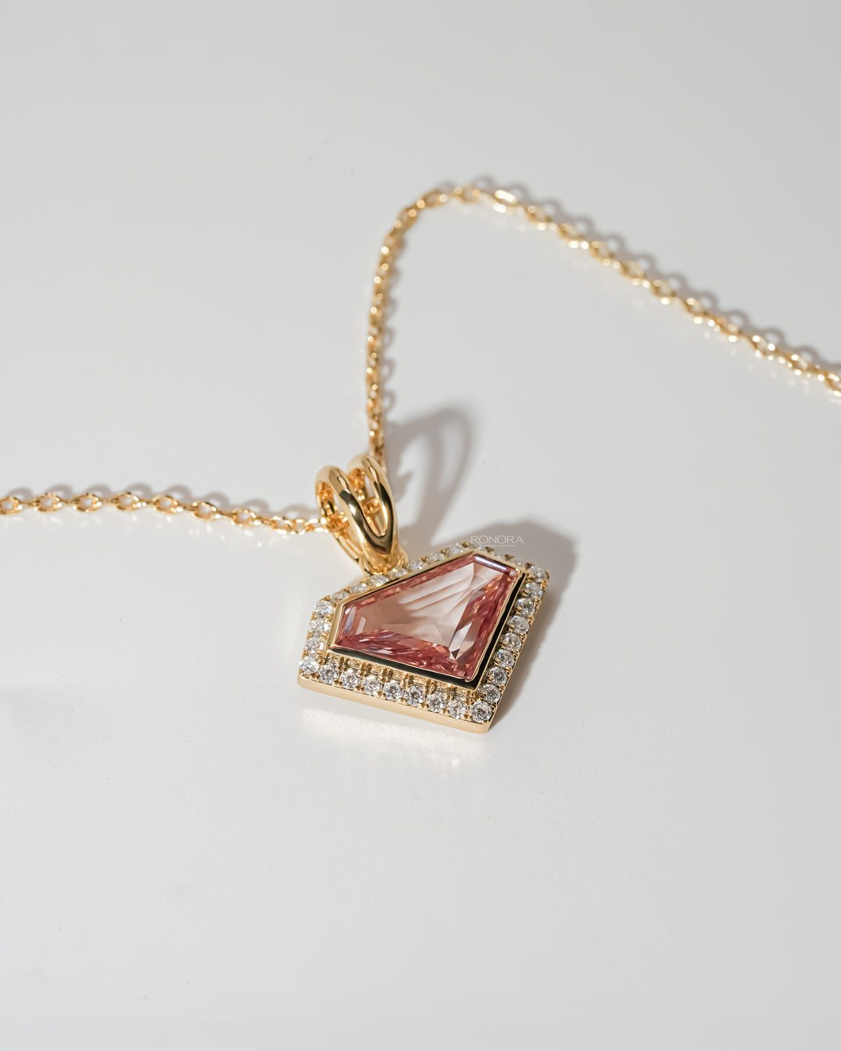 Angled view of a pink shield cut lab grown diamond necklace with a white stone halo and yellow gold chain