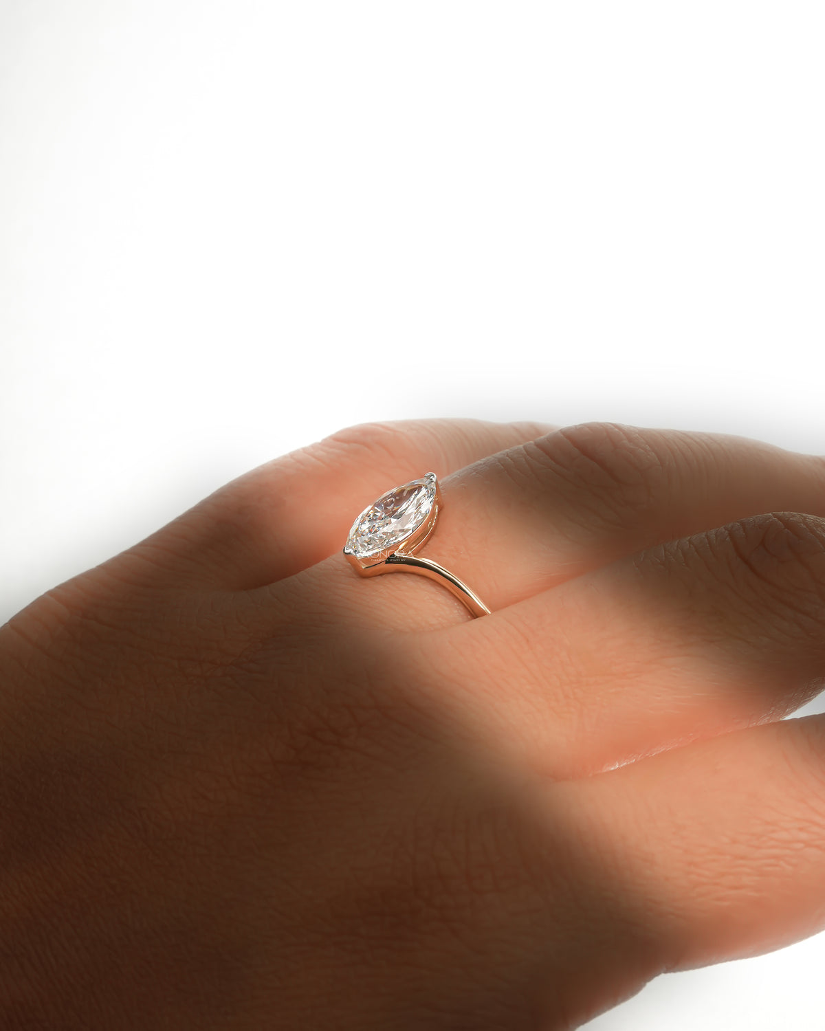 Side view of a marquise lab grown diamond bypass ring on a hand, gold band sweeping up to the stone